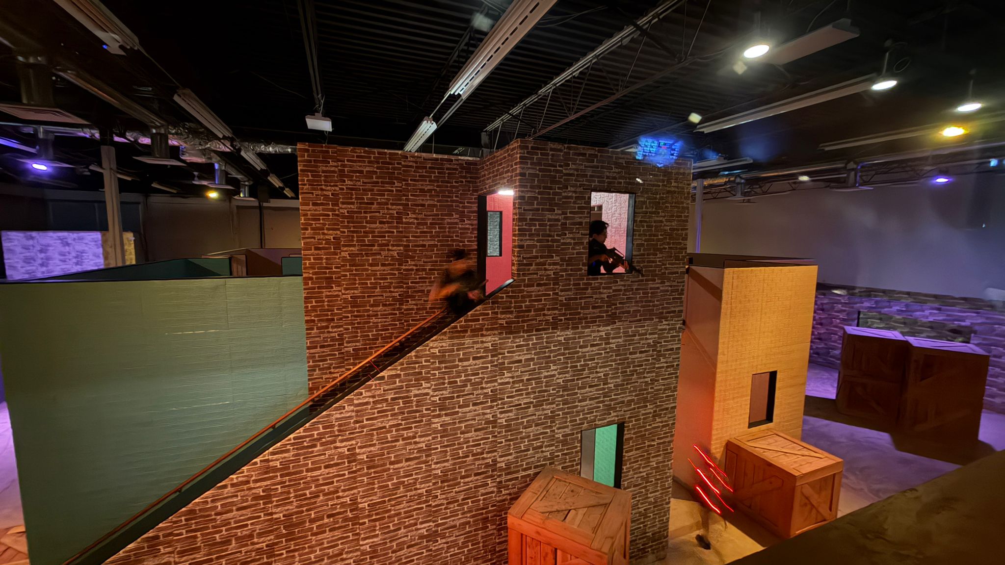 Jack in a laser tag arena, vest lit up, taking cover behind a barrier.